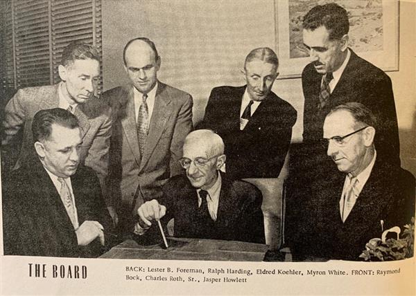 Board members from 1953, seated and standing near a table